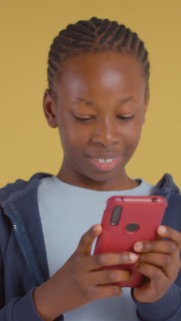 Vertical-Video-Of-Boy-On-ASD-Spectrum-Gaming-On-Mobile-Phone-On-Yellow-Background-In-Studio